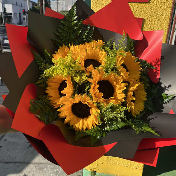 Hand-tied bouquet of yellow sunflowers with filler flowers wrapped in red and black paper.