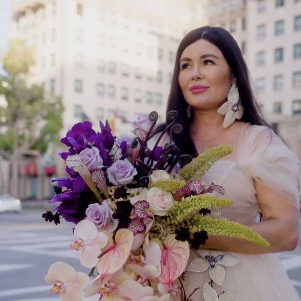Woman in a pale gown holding a large bouquet of orchids and roses