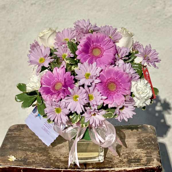 Pink gerberas and daisies arranged in a clear glass vase with a ribbon.