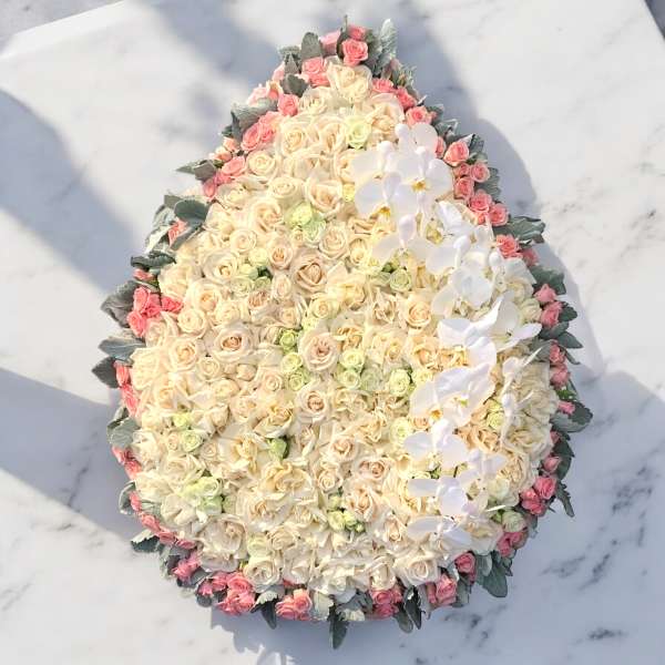 Large oval arrangement of cream and pink roses with white orchids