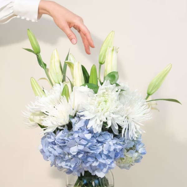 White lilies and blue hydrangeas arranged in a glass vase