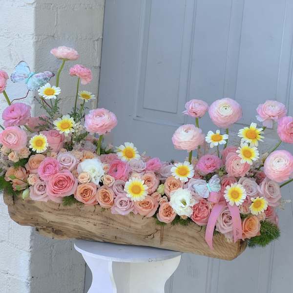 Pink and peach flower arrangement in a wooden container with daisies and butterflies
