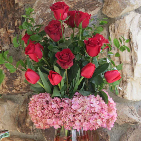 Red roses and pink hydrangeas in a tall glass vase