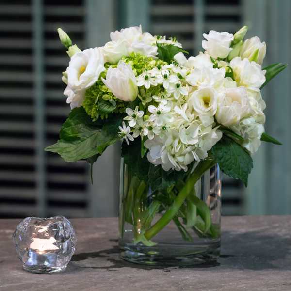 White flowers arranged in a clear glass vase beside a small candle holder