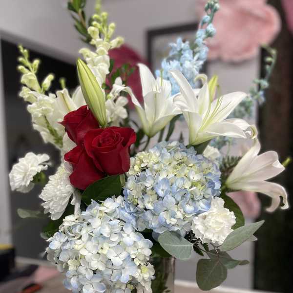 Bouquet of red roses, white lilies, and blue hydrangeas in a glass vase