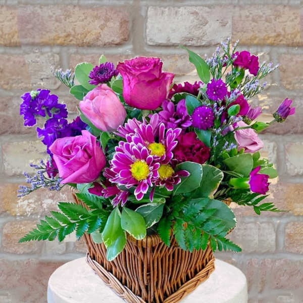 Pink and purple mixed flower arrangement in a rectangular wicker basket