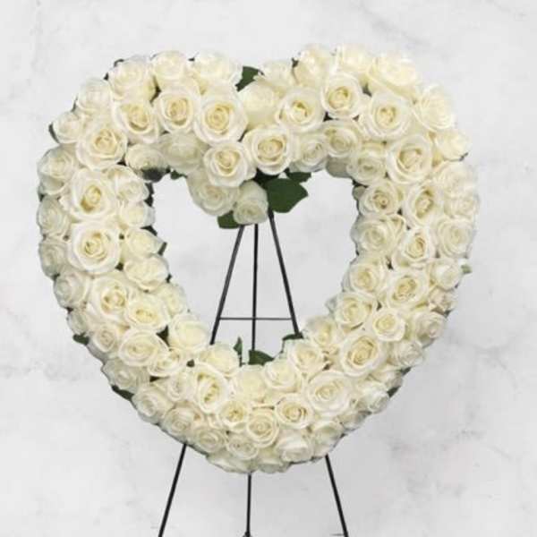 Heart-shaped white rose wreath on a black stand with a white bow