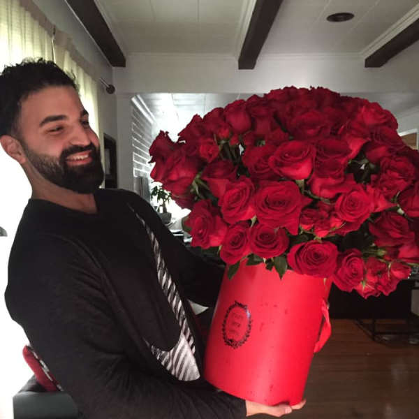 Man holding an oversized red hatbox filled with many red roses.