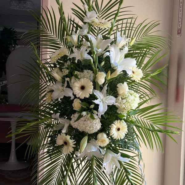 White funeral spray with lilies, gerberas, and palm fronds