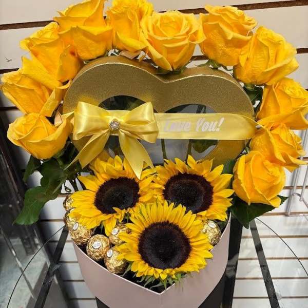 Yellow roses and sunflowers arranged in a heart-shaped box with a ribbon