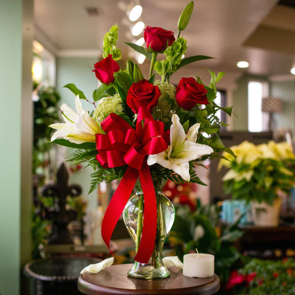 Red roses and white lilies in a clear glass vase with a red bow