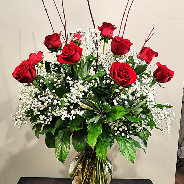 Tall arrangement of red roses and white filler flowers in a clear glass vase on a dark table