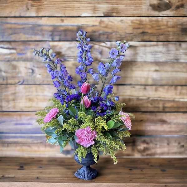 Purple and pink floral arrangement in a dark pedestal vase