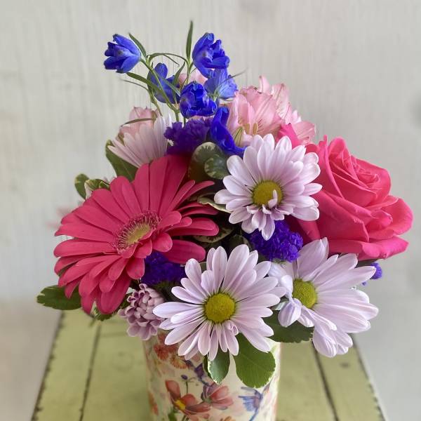 Mixed pink and purple flowers in a floral tin vase
