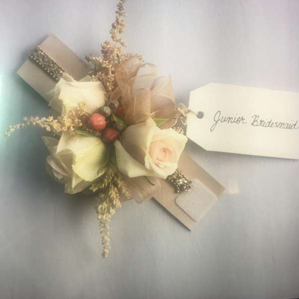 Small corsage with cream roses and a name tag reading Junior Bridesmaid