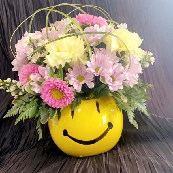 Pink and yellow daisy bouquet in a yellow smiley-face container