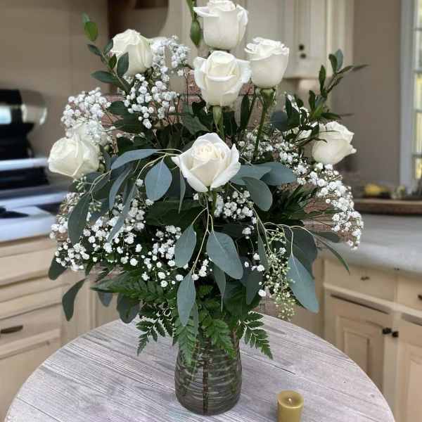 White roses arranged in a glass vase with baby's breath and greenery