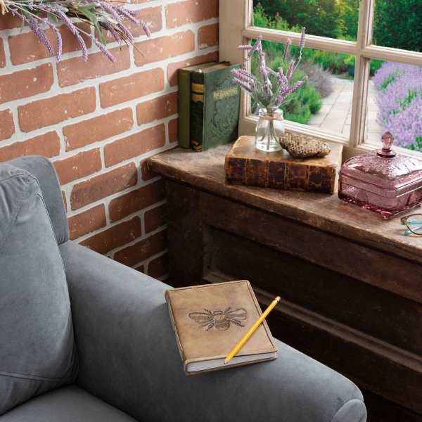A small vase of purple flowers sits on a wooden table by a window.