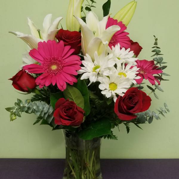 Bouquet of red roses, pink gerberas, white lilies, and daisies in a glass vase