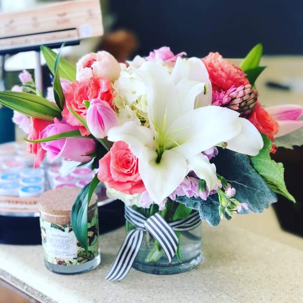 Pink and white flower arrangement in a glass vase with a striped ribbon