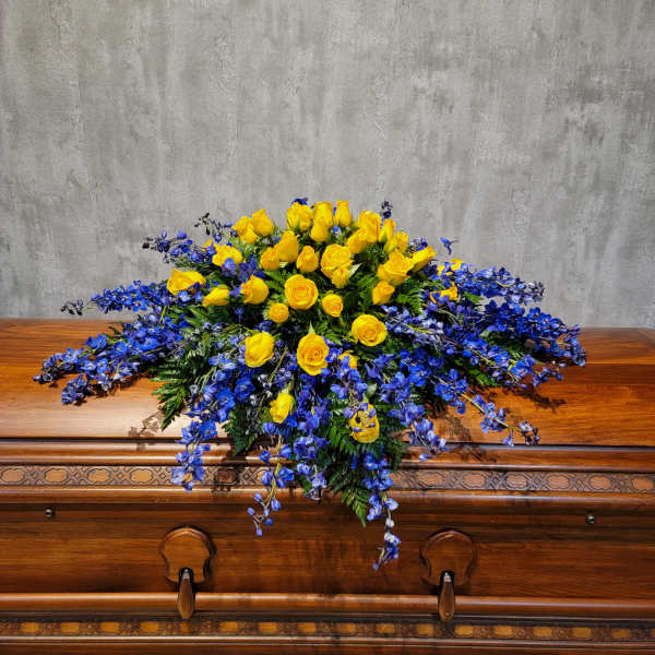 Yellow roses and blue flowers arranged on a wooden casket