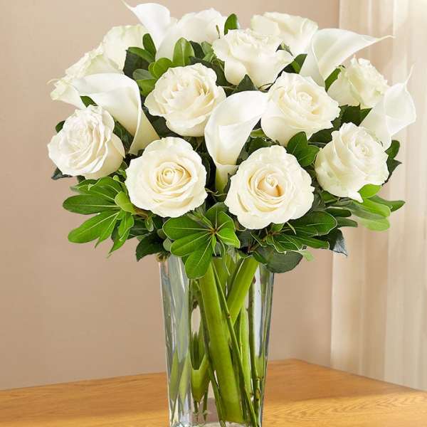White roses and calla lilies arranged in a clear glass vase