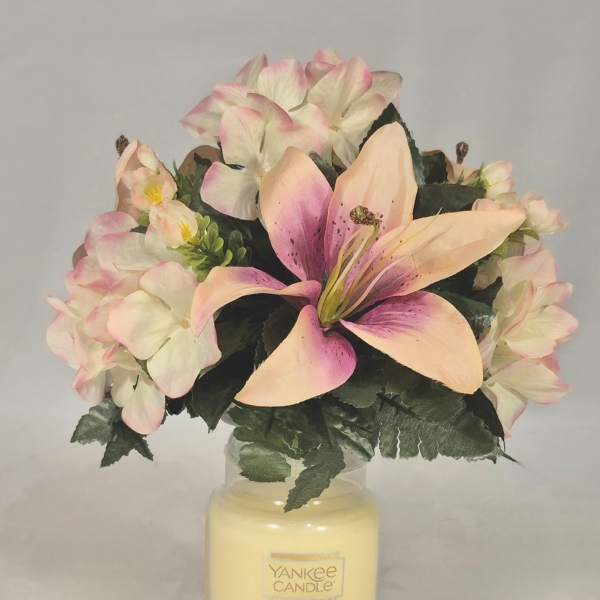 Pink and cream flowers arranged in a glass candle jar