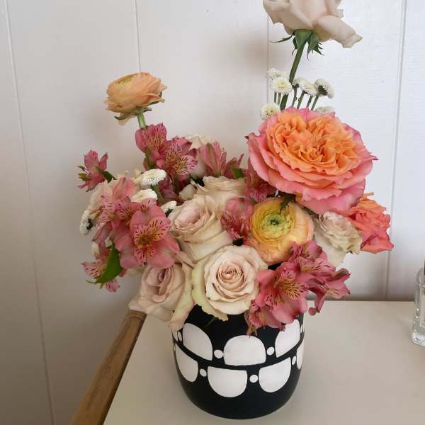 Mixed pink and cream flowers arranged in a black vase with white dots