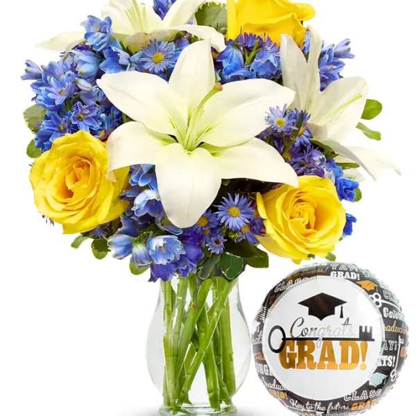 Bouquet of white lilies, yellow roses, and blue flowers in a glass vase with a graduation balloon
