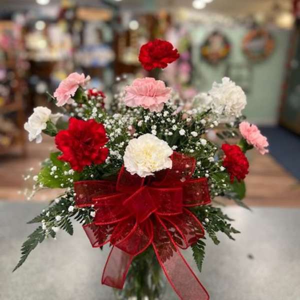 Bouquet of red, pink, and white carnations in a glass vase with a red ribbon
