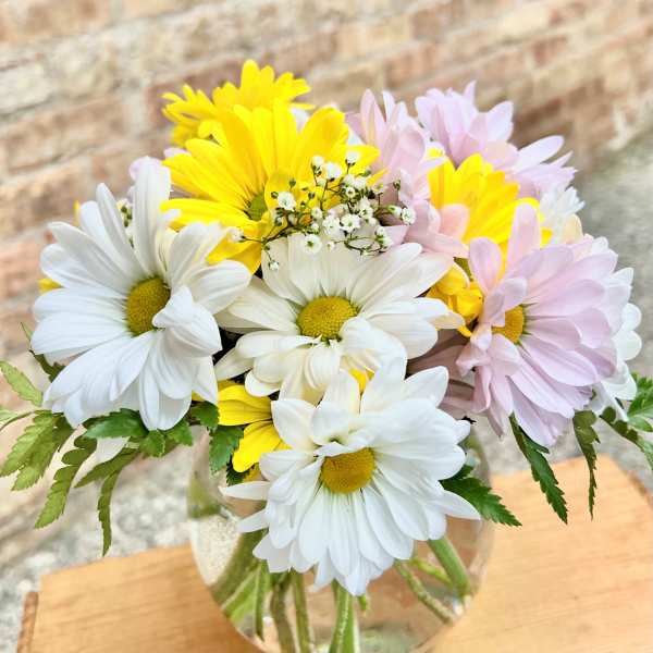 Bouquet of white, yellow, and pale pink daisies in a glass vase