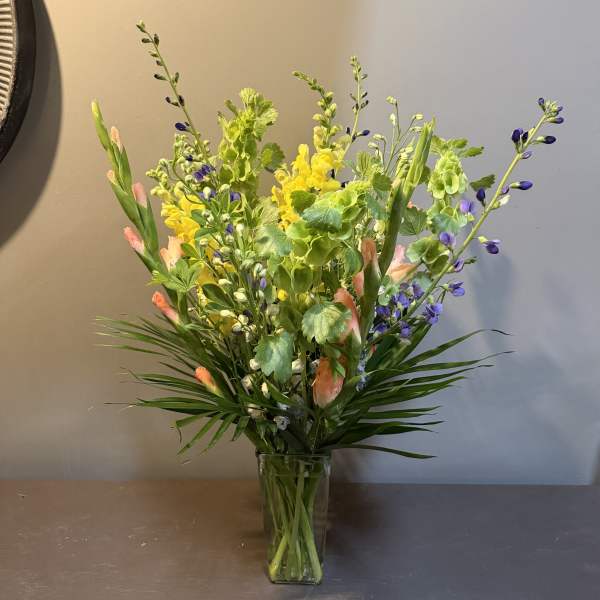 Tall mixed bouquet in a clear glass vase with yellow, purple, and peach blooms