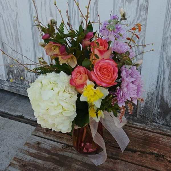 Mixed bouquet with roses, hydrangea, and daffodils in a glass vase