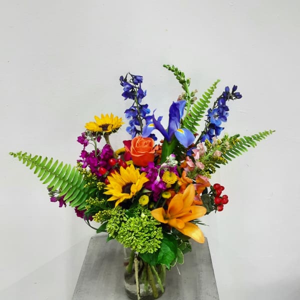 Colorful mixed bouquet in a clear glass vase with sunflowers, roses, and blue flowers