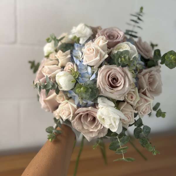 Handheld bouquet of blush roses, white blooms, and blue flowers