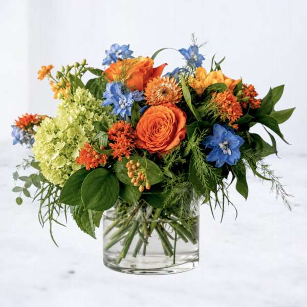 Orange and blue mixed flower arrangement in a clear glass vase