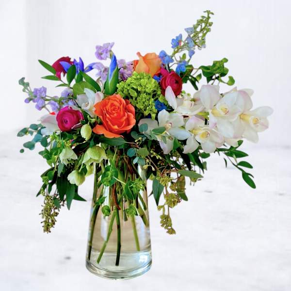 Mixed bouquet of roses, orchids, and blue flowers in a glass vase