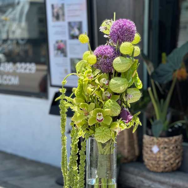 Tall vase arrangement with green orchids and purple allium