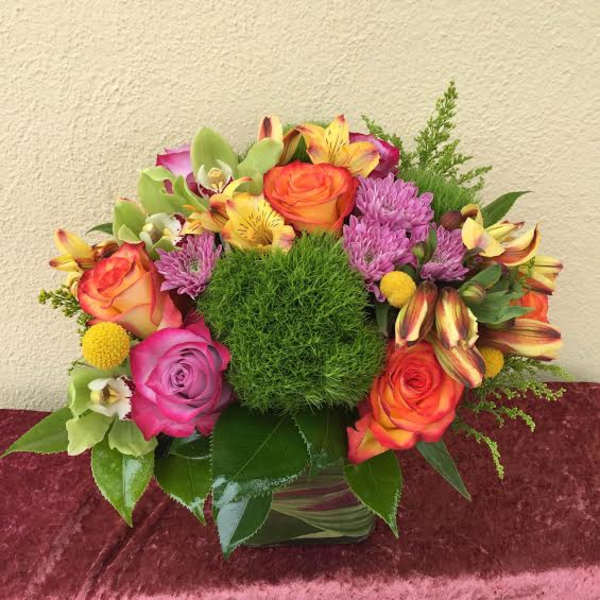 Colorful bouquet with roses, orchids, and purple blooms in a glass vase