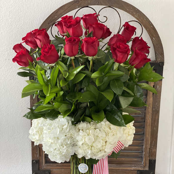 Red roses above white hydrangeas in a glass vase with a striped ribbon