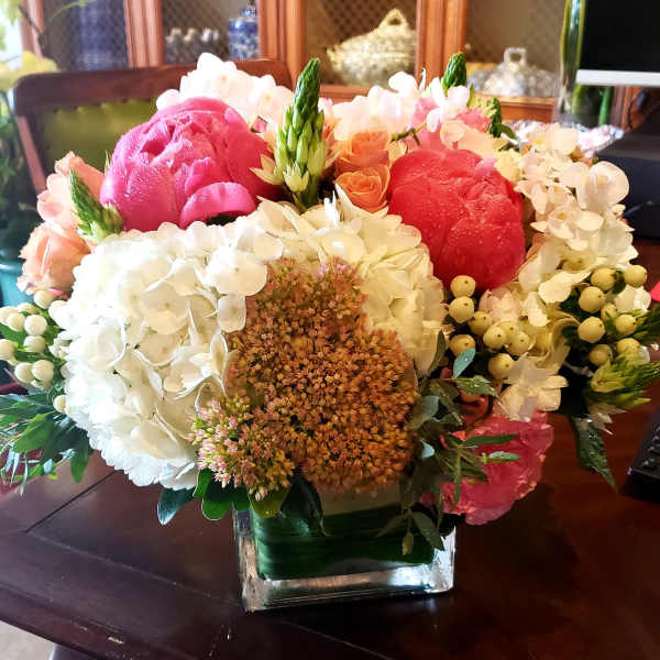 Mixed bouquet of pink, red, white, and peach flowers in a square glass vase