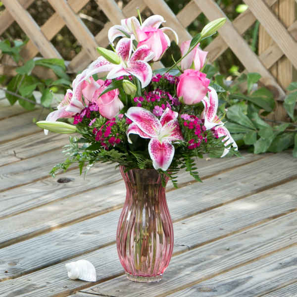 Pink lilies and roses arranged in a pink glass vase