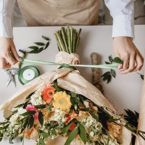 Person tying ribbon around a wrapped bouquet of mixed flowers