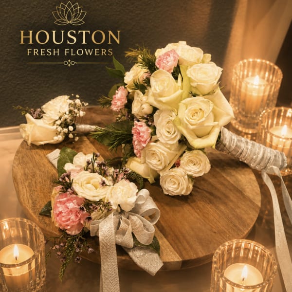 Cream and pink rose bouquets with ribbon on a wooden table beside candles
