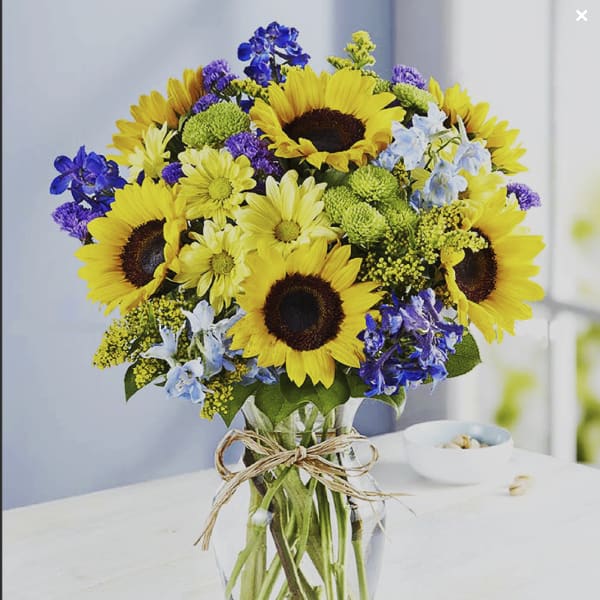 Bouquet of sunflowers, blue flowers, and purple accents in a glass vase