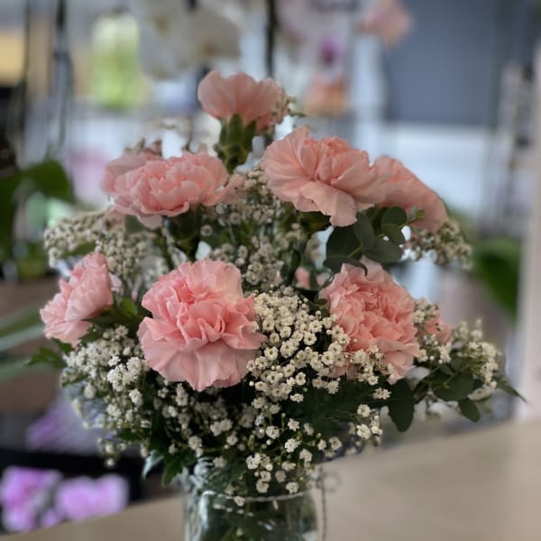 Pink carnation and white filler flower bouquet arranged in a clear glass jar
