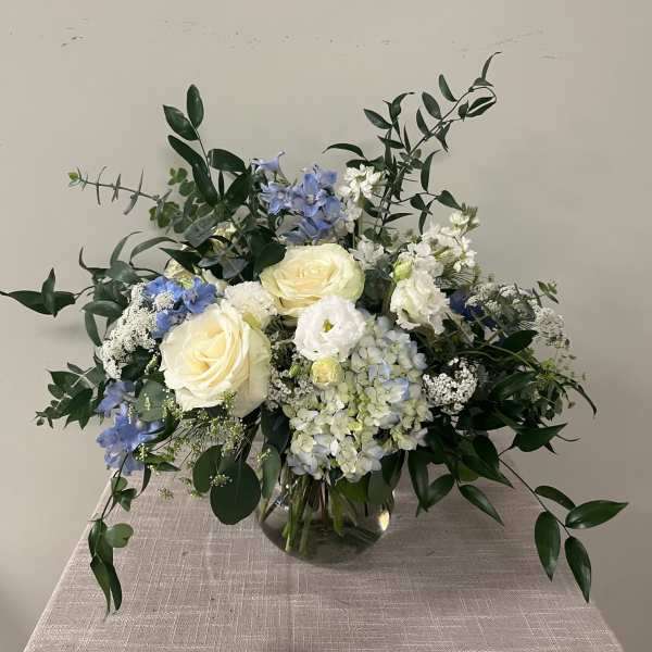 Bouquet of white roses, blue flowers, and greenery in a glass vase