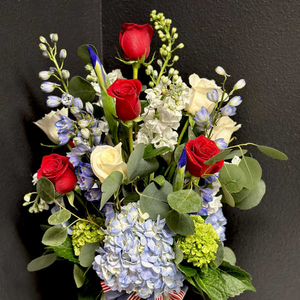 Bouquet of red and white roses with blue flowers in a glass vase