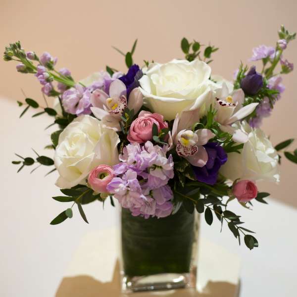 Bouquet of white roses, pink blooms, and purple flowers in a glass vase