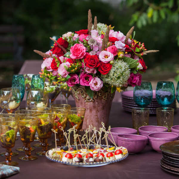 Large pink and red floral centerpiece on a table with glassware and desserts